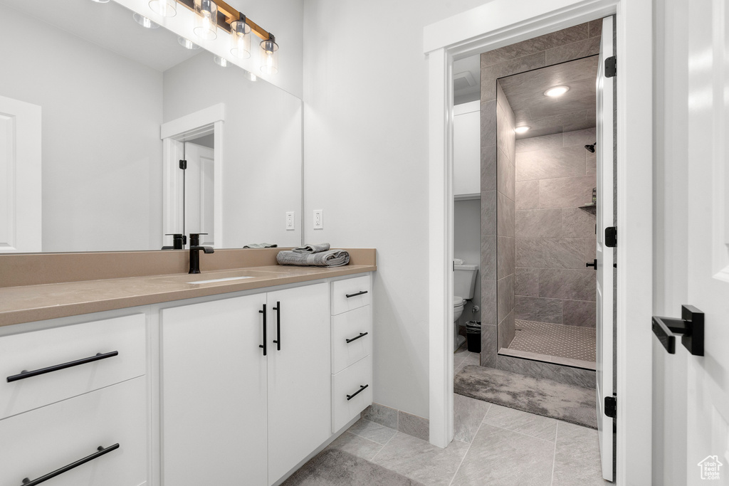 Bathroom with baseboards, tiled shower, toilet, and vanity