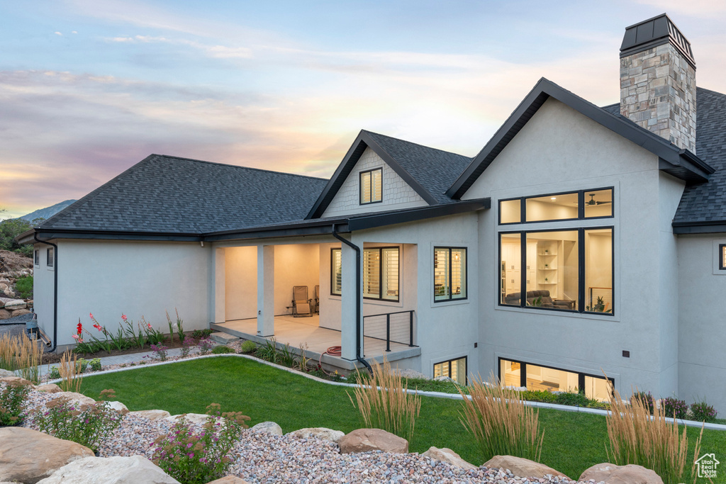 Rear view of property with a yard, stucco siding, a shingled roof, and a patio