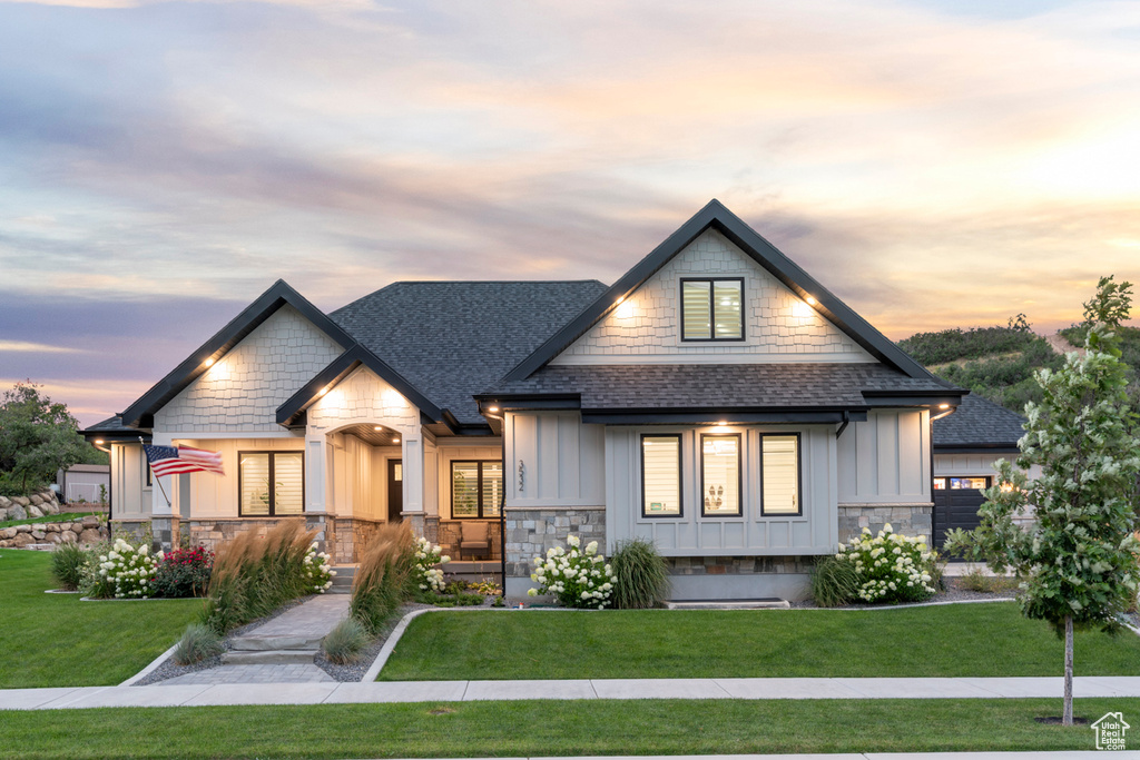 View of front facade featuring stone siding, board and batten siding, a shingled roof, and a front yard