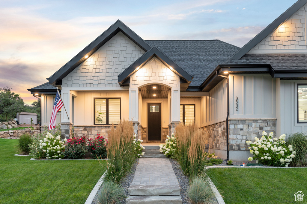 View of front of house with board and batten siding, a yard, stone siding, and a shingled roof