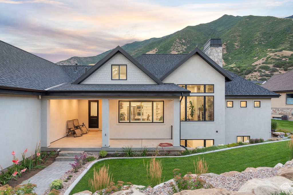 Back of property at dusk featuring a mountain view, stucco siding, a porch, and a shingled roof