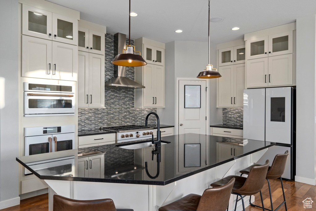 Kitchen with a breakfast bar area, white cabinets, white appliances, wall chimney exhaust hood, and a sink