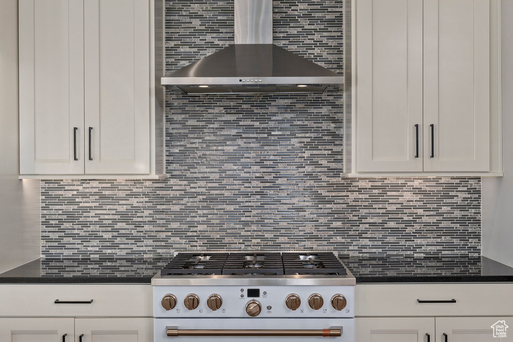 Kitchen featuring dark countertops, wall chimney range hood, tasteful backsplash, and white gas range