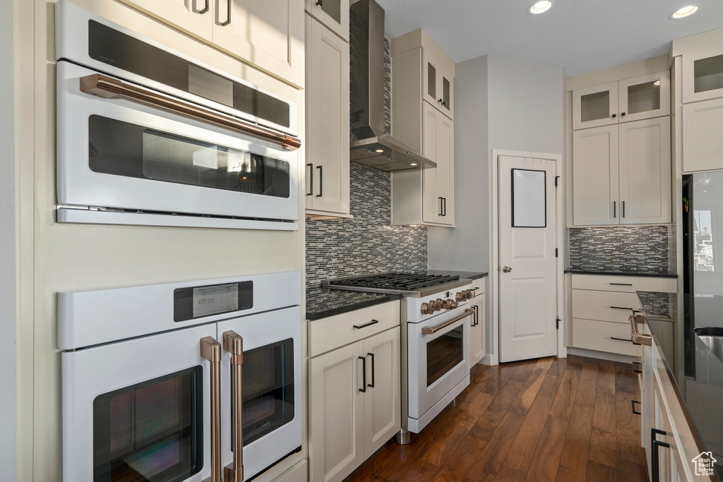 Kitchen with dark wood-style floors, tasteful backsplash, glass insert cabinets, and wall chimney range hood