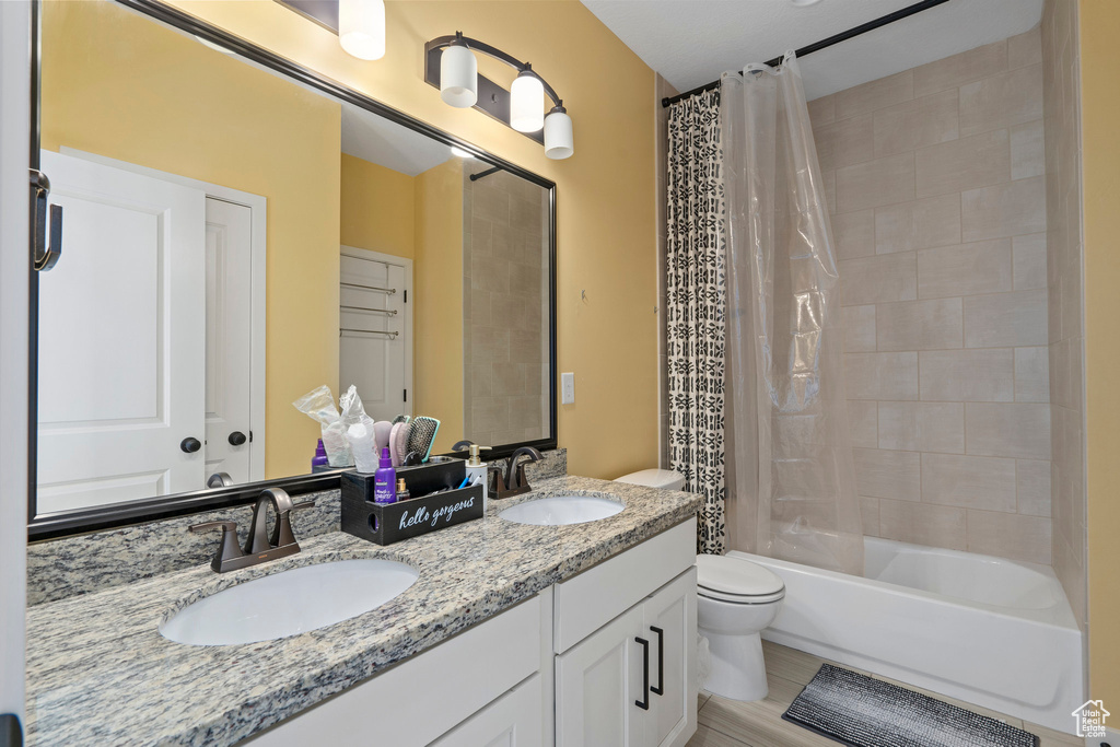Full bath featuring double vanity, shower / bath combination with curtain, toilet, and a sink