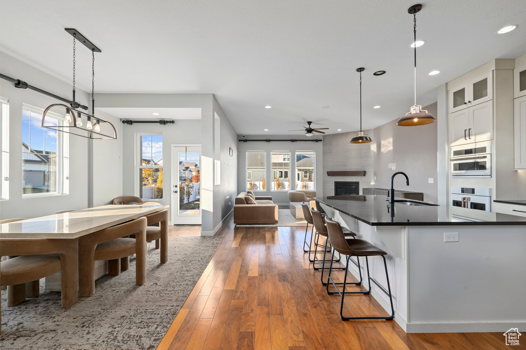 Kitchen with a sink, dark countertops, white cabinetry, a large fireplace, and wood-type flooring
