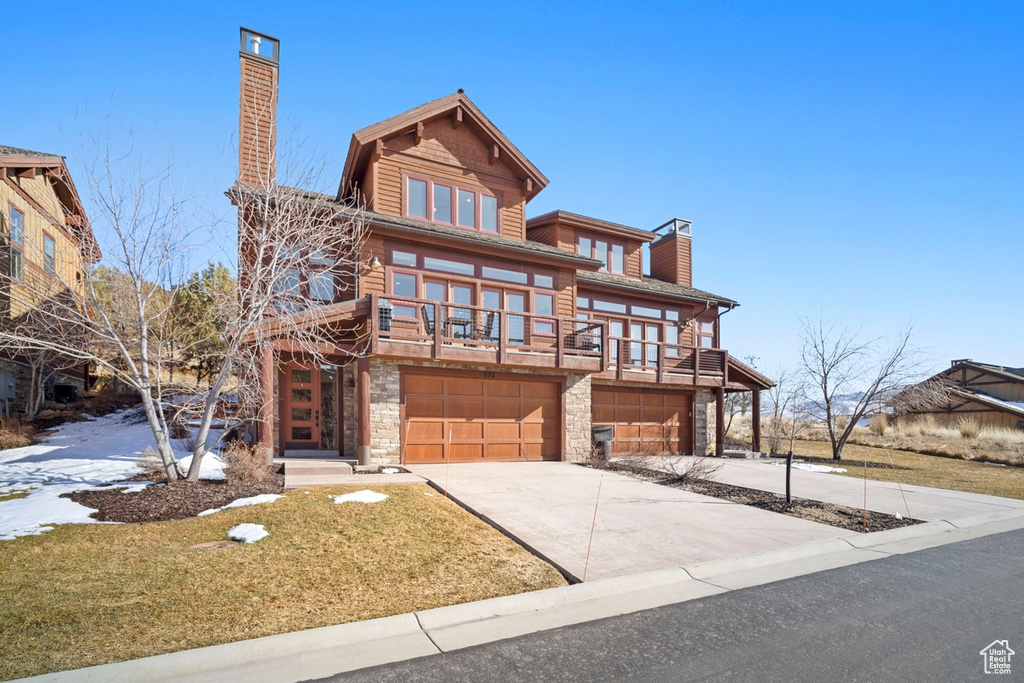 View of front of home featuring a chimney, stone siding, an attached garage, concrete driveway, and a front lawn