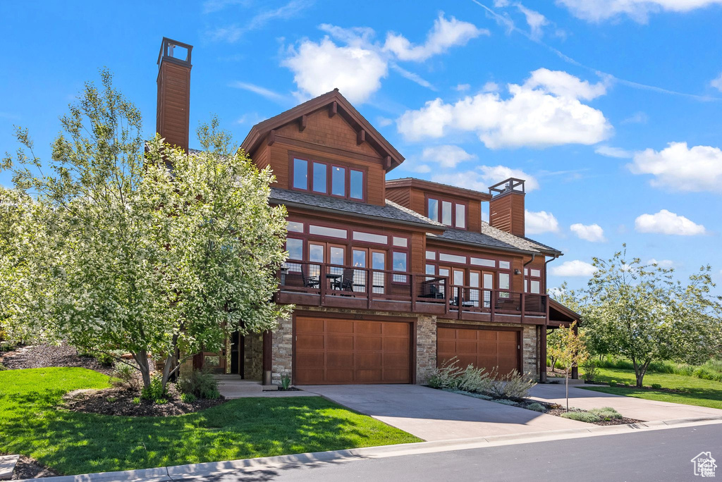 View of front of property featuring a chimney, stone siding, an attached garage, driveway, and a front yard