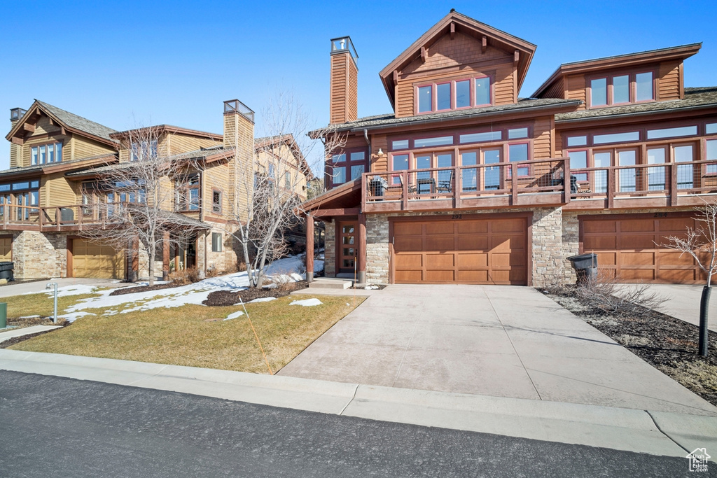 View of front facade featuring stone siding, an attached garage, driveway, and a balcony