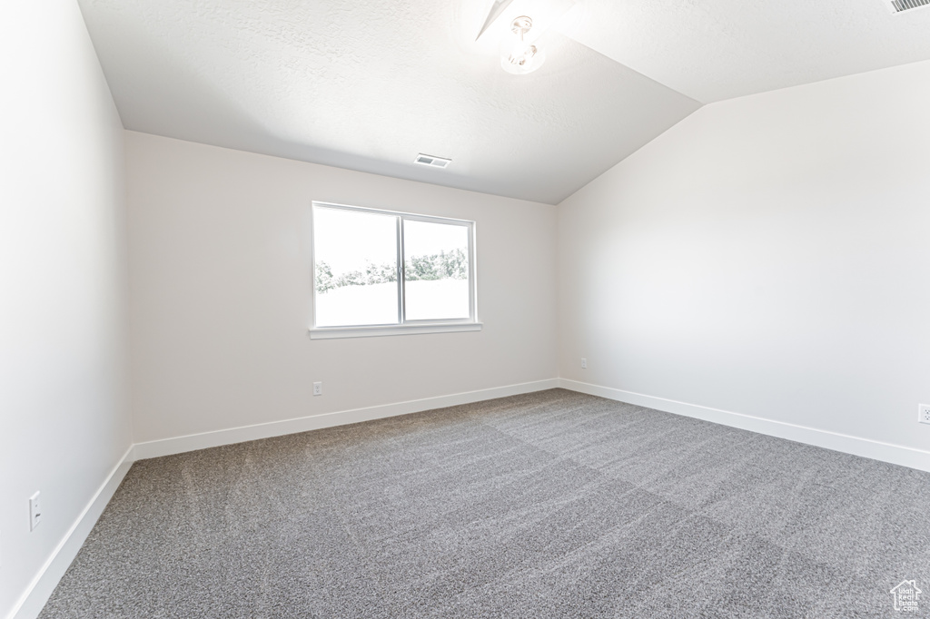 Carpeted empty room with lofted ceiling and baseboards