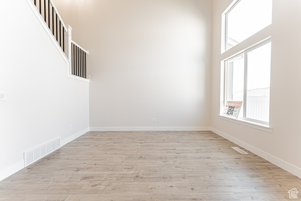 Empty room with healthy amount of natural light, light wood finished floors, and a towering ceiling