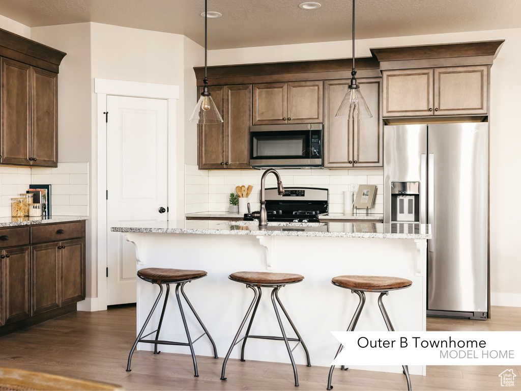 Kitchen featuring light stone countertops, dark wood-type flooring, appliances with stainless steel finishes, and a breakfast bar area