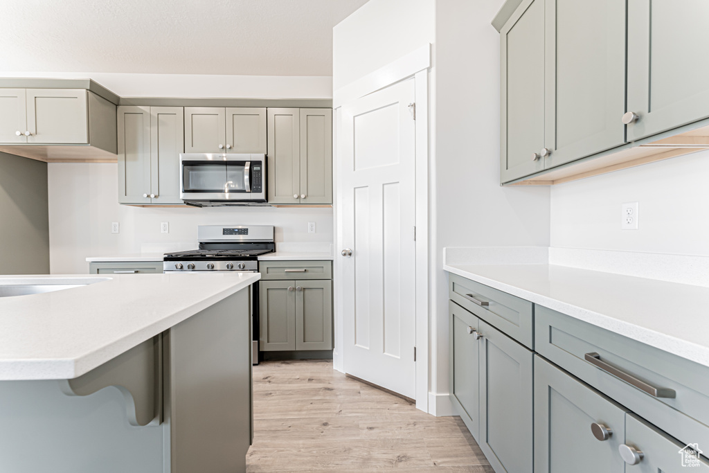 Kitchen featuring appliances with stainless steel finishes, gray cabinets, light wood-type flooring, light countertops, and a breakfast bar
