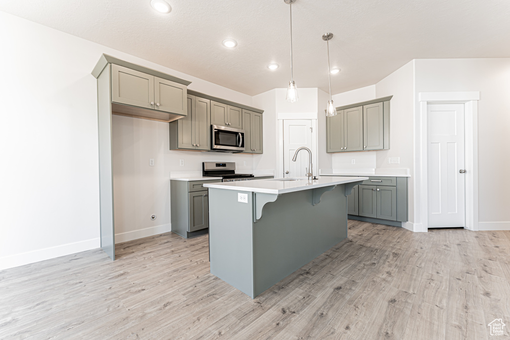 Kitchen featuring stainless steel appliances, gray cabinetry, a breakfast bar, light wood-style floors, and recessed lighting
