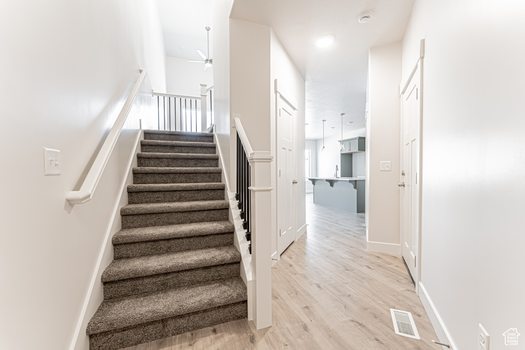 Stairs with a ceiling fan and wood finished floors