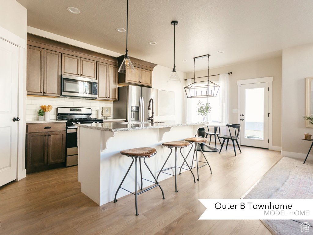 Kitchen with a breakfast bar area, light stone countertops, a kitchen island with sink, stainless steel appliances, and decorative backsplash