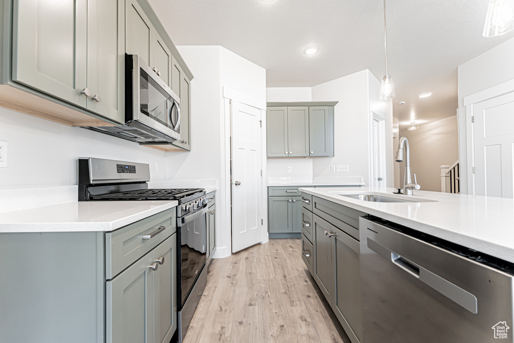 Kitchen featuring appliances with stainless steel finishes, gray cabinetry, light wood-style floors, decorative light fixtures, and light countertops