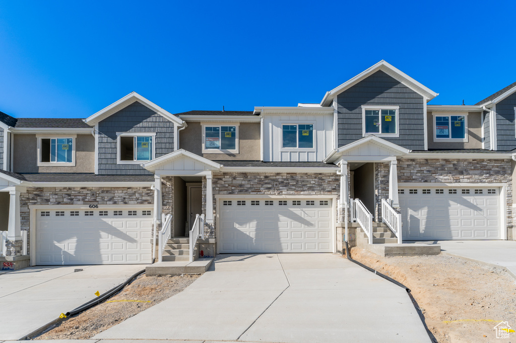 Townhome / multi-family property with an attached garage, driveway, and stone siding