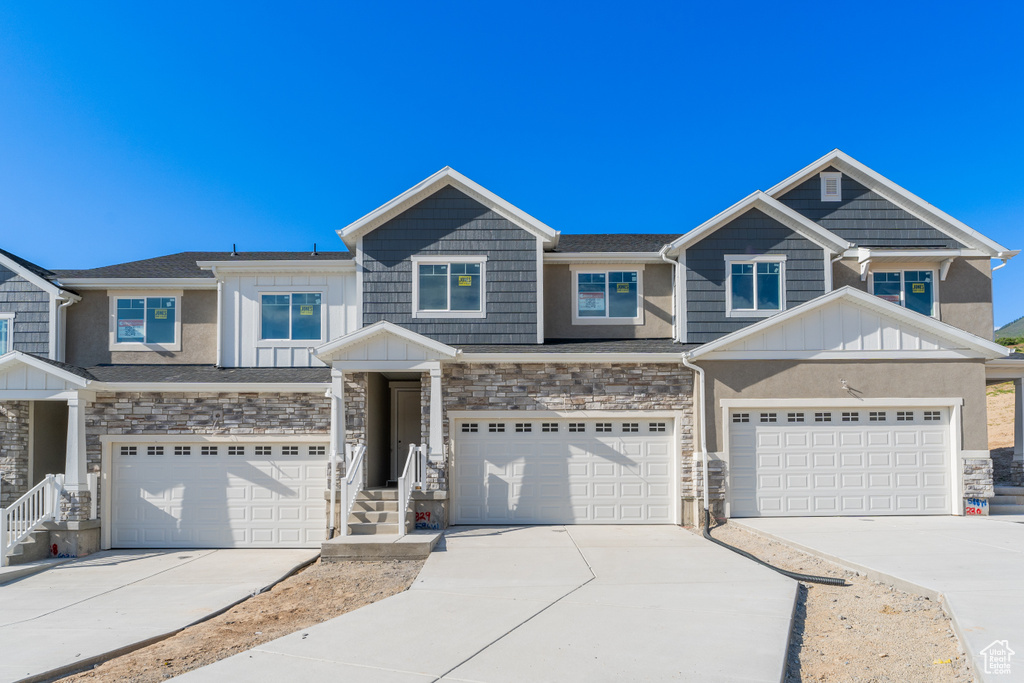 Multi unit property featuring board and batten siding, driveway, a garage, and stone siding