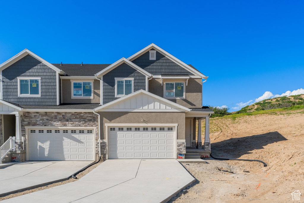 View of front of property featuring stone siding, concrete driveway, an attached garage, and board and batten siding