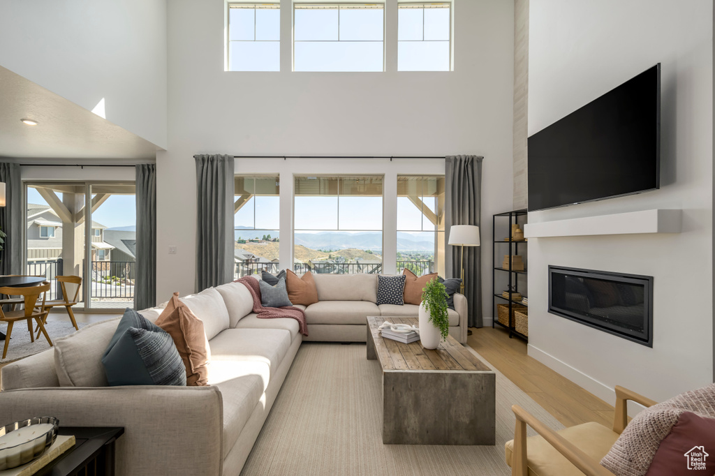 Living area featuring a glass covered fireplace, plenty of natural light, light wood finished floors, and a towering ceiling