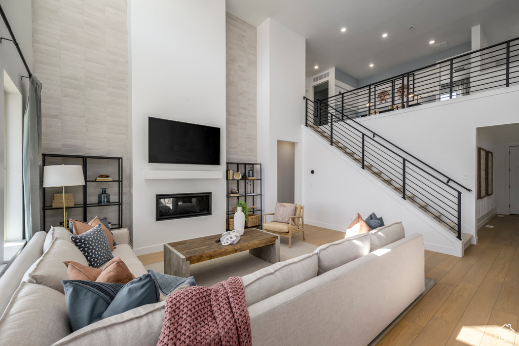 Living room with stairway, baseboards, a high ceiling, hardwood / wood-style flooring, and a glass covered fireplace