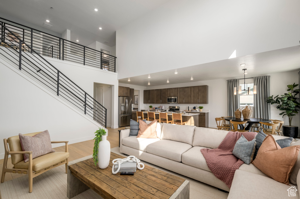 Living area featuring stairs, recessed lighting, light wood-style flooring, a high ceiling, and an inviting chandelier