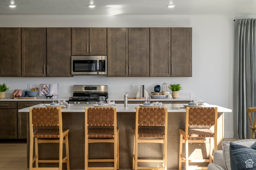 Kitchen featuring a kitchen bar, dark brown cabinets, appliances with stainless steel finishes, and light countertops