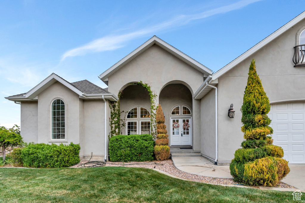 View of front of home featuring a garage, french doors, a front lawn, and stucco siding