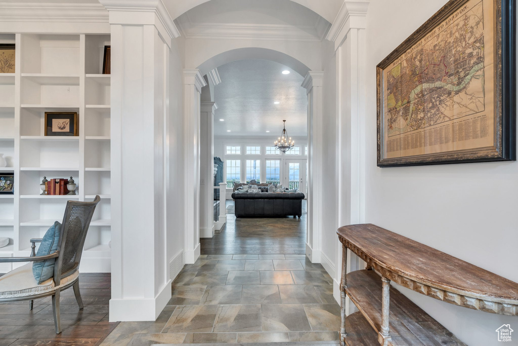 Hall with arched walkways, baseboards, an inviting chandelier, ornamental molding, and ornate columns