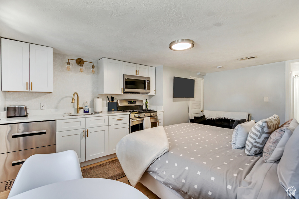 Bedroom with a sink, visible vents, light wood-style floors, and a textured ceiling