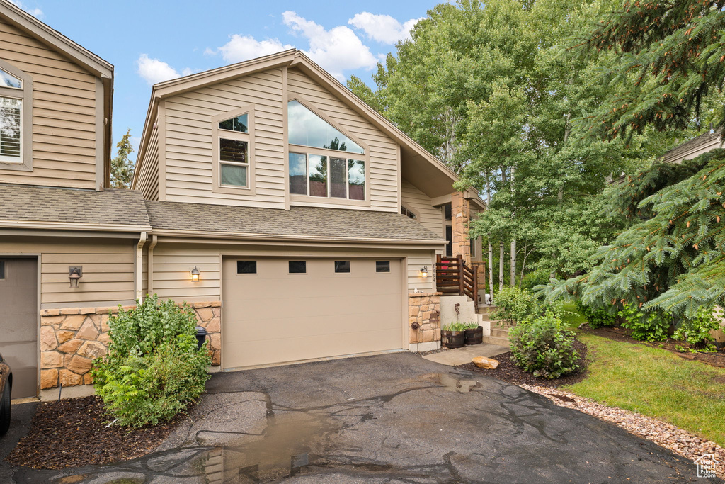 View of front facade featuring an attached garage, asphalt driveway, stone siding, and roof with shingles
