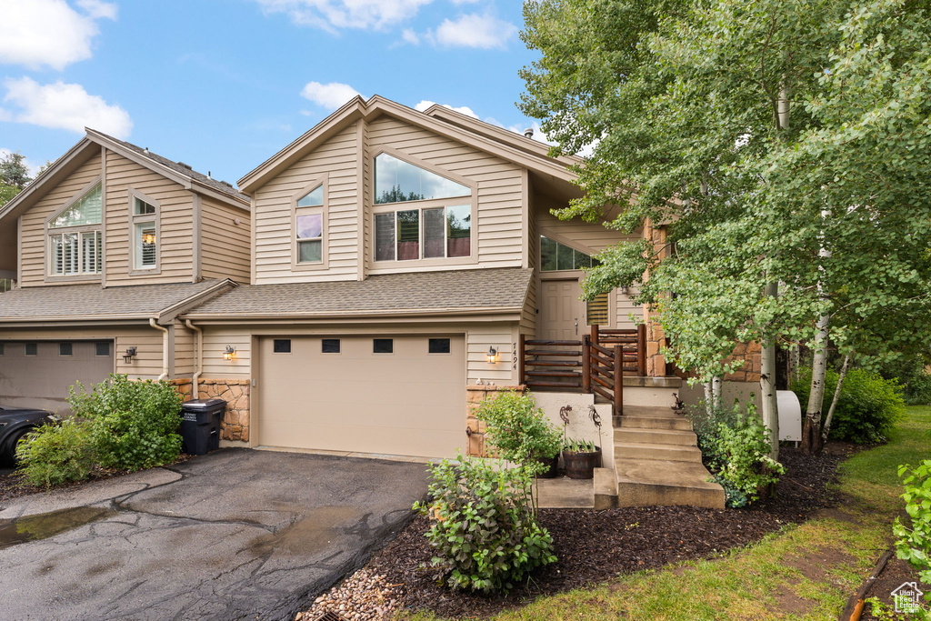View of front of home with a garage, asphalt driveway, stone siding, and a shingled roof