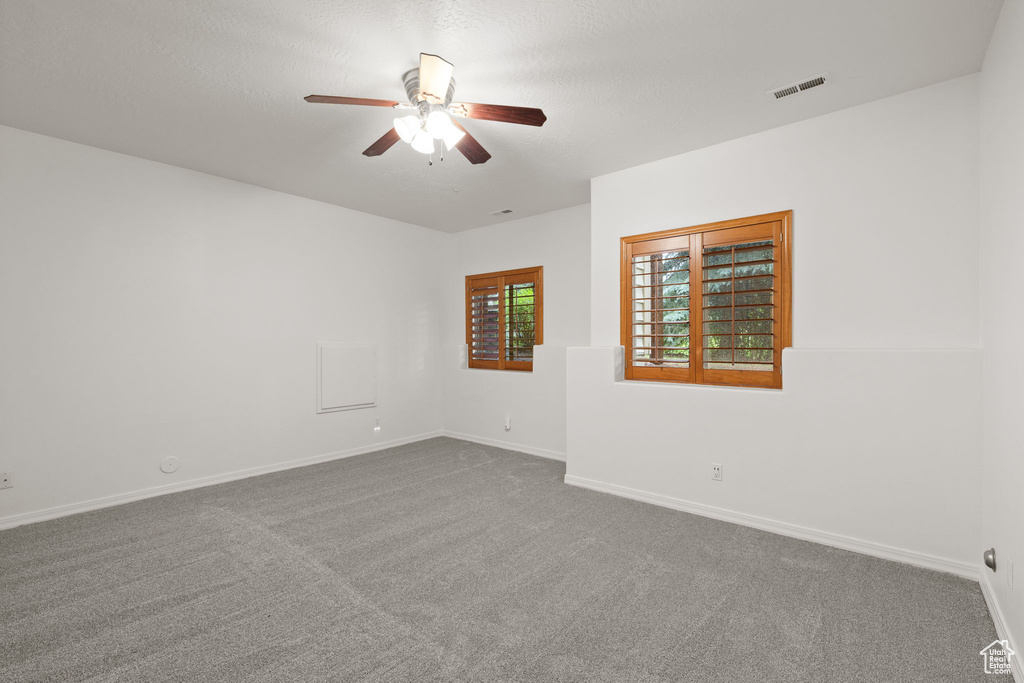 Empty room with a ceiling fan and dark colored carpet