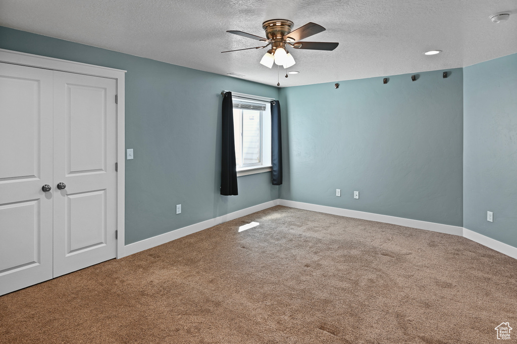 Unfurnished bedroom with a textured ceiling, carpet flooring, baseboards, a closet, and a ceiling fan