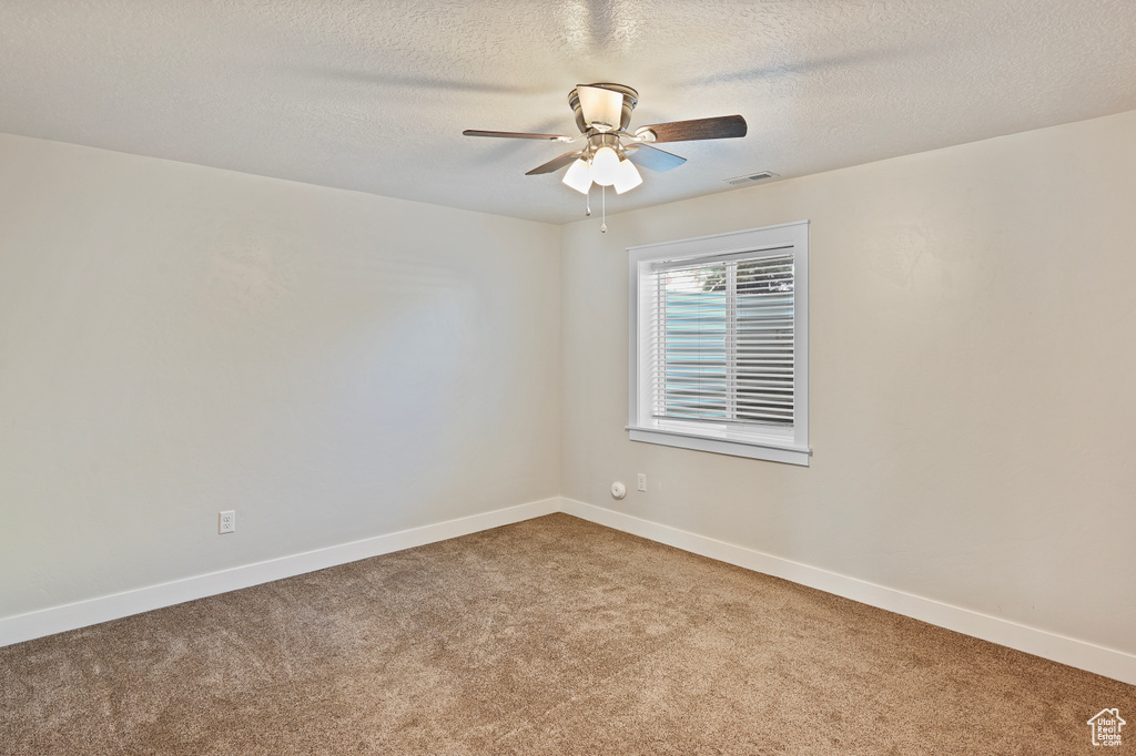 Carpeted empty room with ceiling fan, baseboards, and a textured ceiling