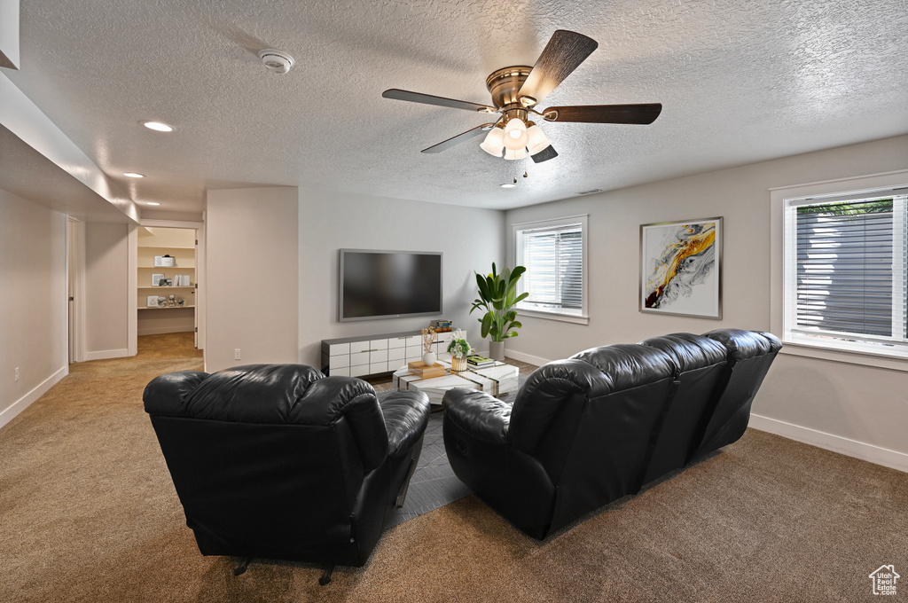 Carpeted living area with baseboards, plenty of natural light, a textured ceiling, and ceiling fan