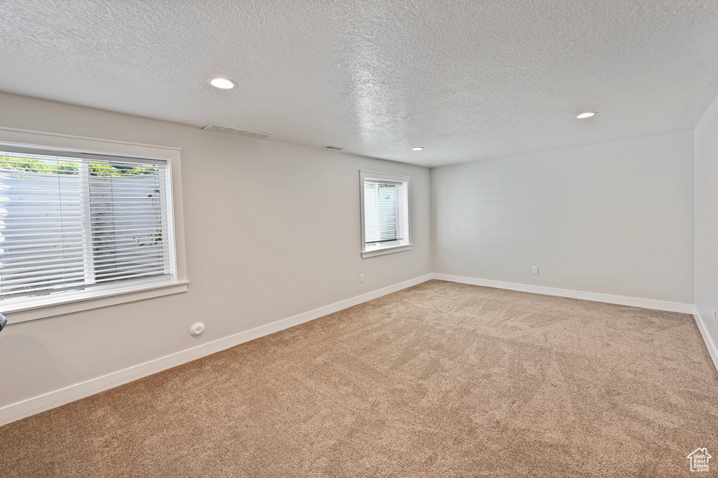 Unfurnished room with a textured ceiling, light carpet, healthy amount of natural light, recessed lighting, and baseboards