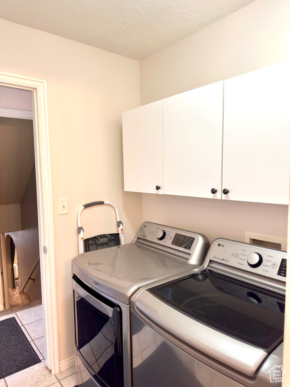 Laundry room featuring washer and dryer, cabinet space, a textured ceiling, and light tile patterned floors