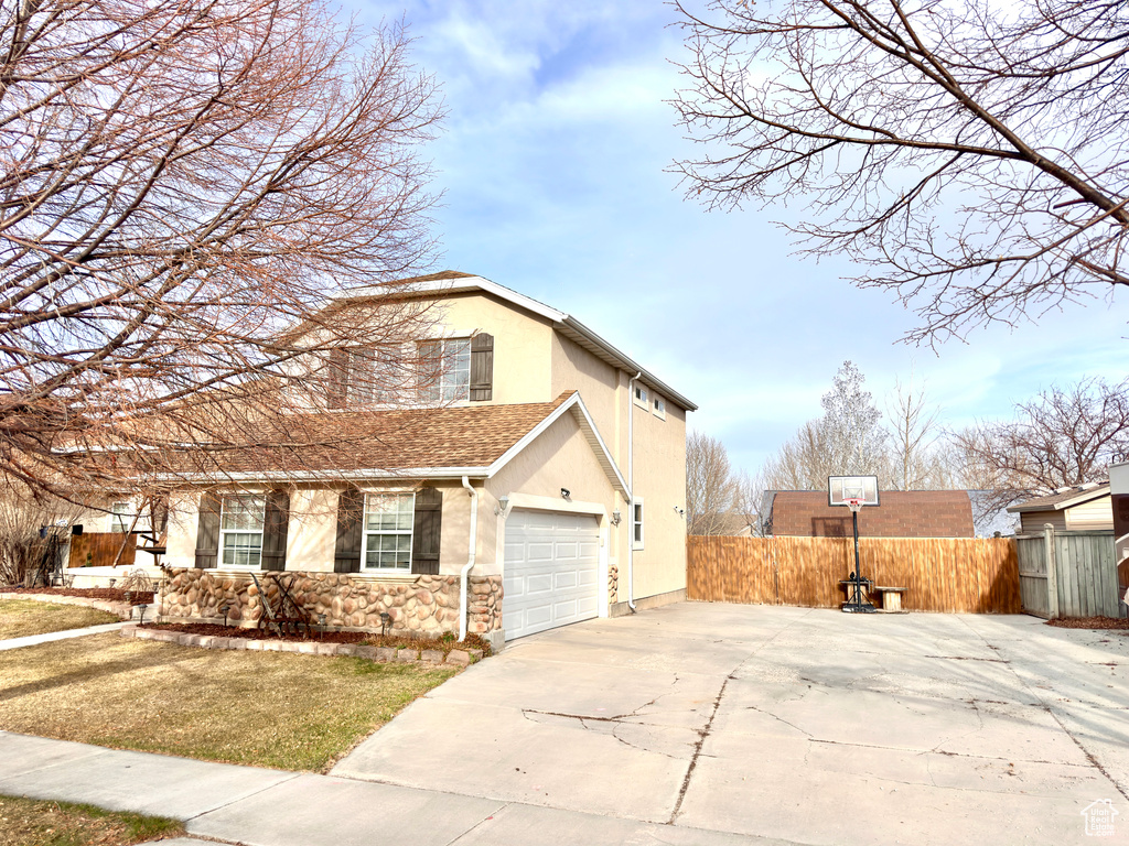 View of property exterior featuring fence, concrete driveway, stucco siding, a garage, and stone siding