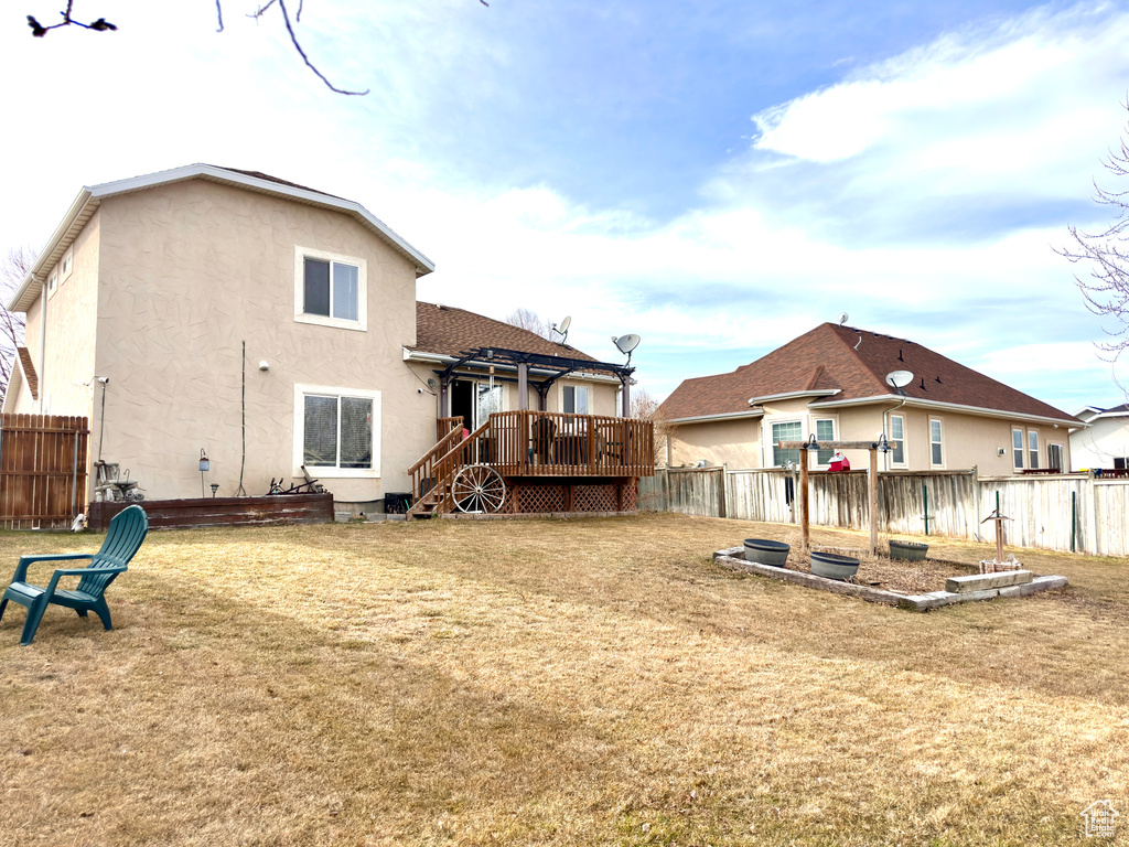 Rear view of house featuring a deck, a yard, fence, and stucco siding