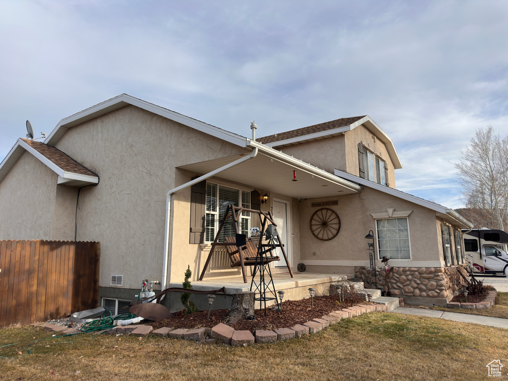 View of front of property with stone siding, stucco siding, a shingled roof, and fence