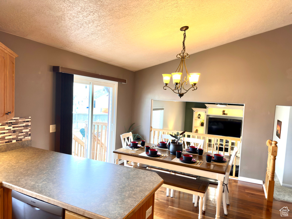 Kitchen with pendant lighting, backsplash, dark wood finished floors, an inviting chandelier, and a peninsula