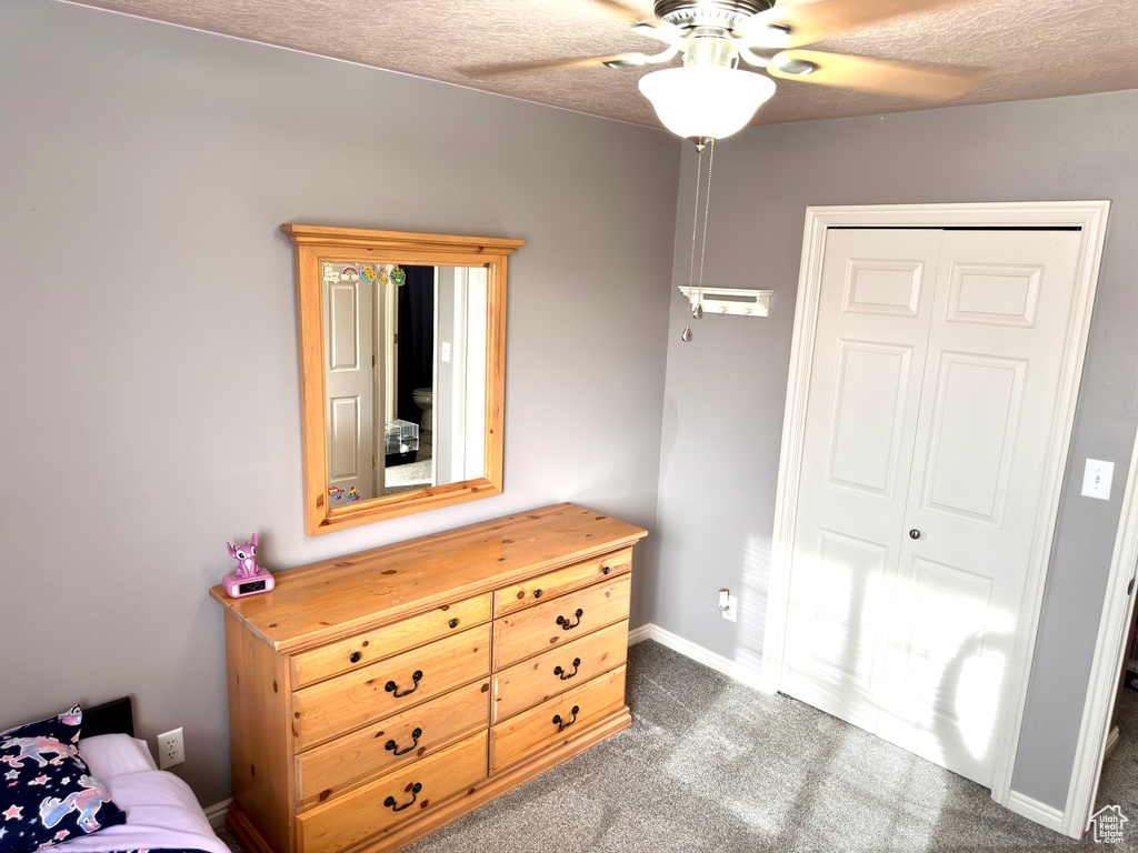 Bedroom featuring baseboards, ceiling fan, a closet, a textured ceiling, and dark colored carpet