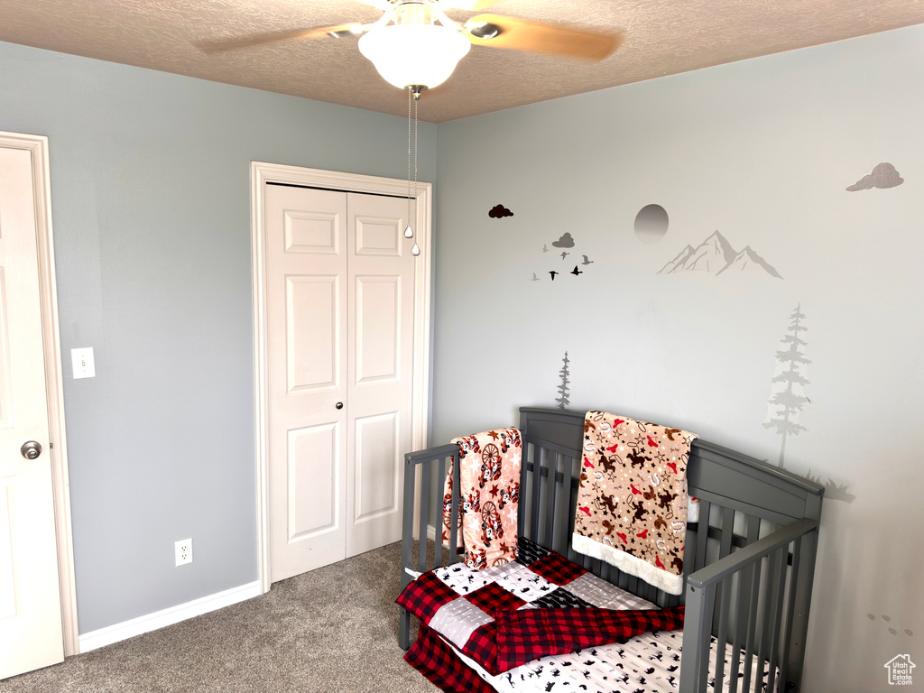 Bedroom featuring a closet, a crib, a textured ceiling, and carpet