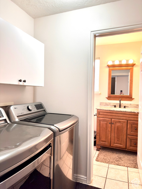 Washroom featuring light tile patterned floors, cabinet space, a sink, a textured ceiling, and independent washer and dryer