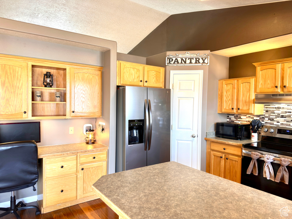 Kitchen featuring light brown cabinetry, under cabinet range hood, stainless steel appliances, decorative backsplash, and vaulted ceiling