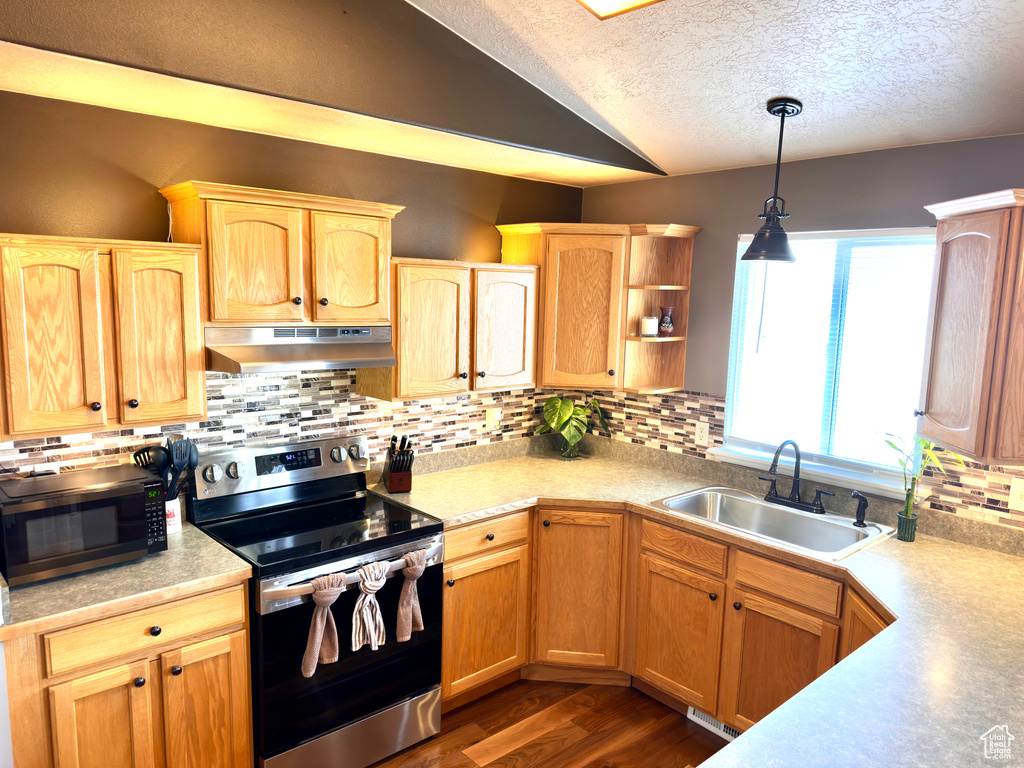 Kitchen with under cabinet range hood, a sink, stainless steel appliances, light countertops, and hanging light fixtures