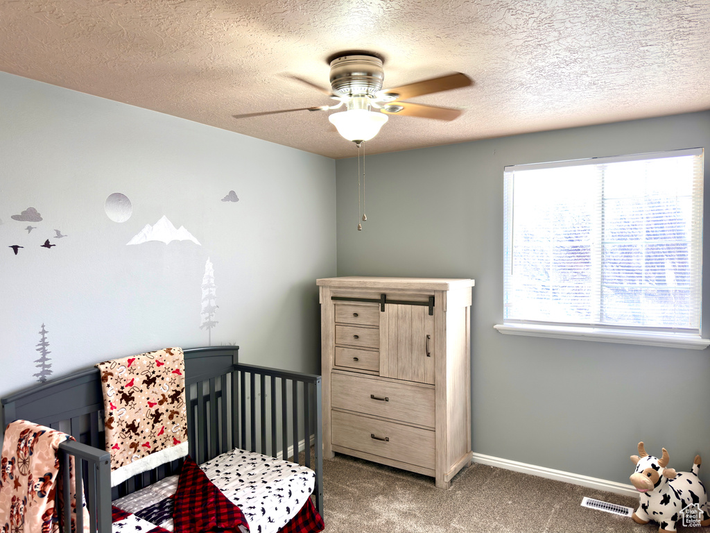 Bedroom with visible vents, baseboards, carpet floors, a nursery area, and a textured ceiling