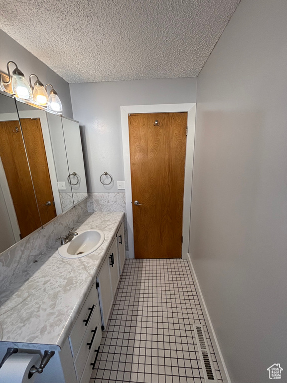 Bathroom with visible vents, baseboards, vanity, tile patterned floors, and a textured ceiling